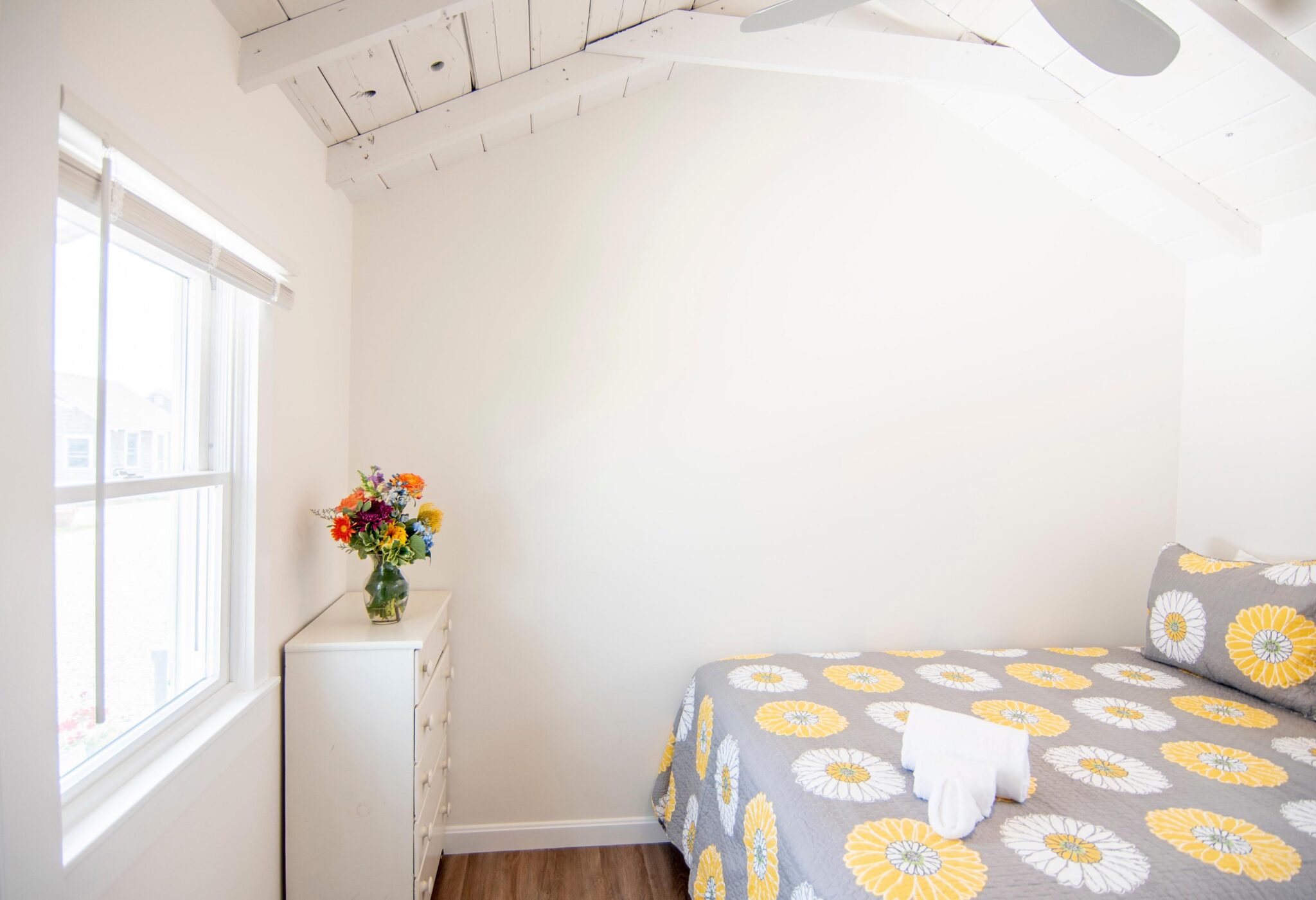 Bright cottage interior with bed and flowers.